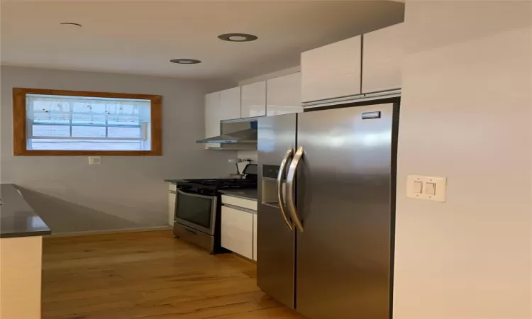 Kitchen with white cabinets, stainless steel appliances, extractor fan, and light wood-type flooring