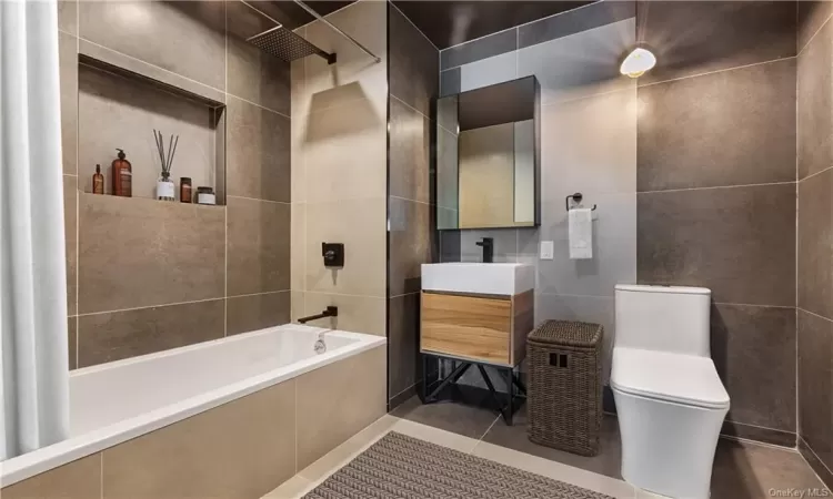 Full bathroom with tile patterned flooring, tile walls, tiled shower / bath combo, and toilet