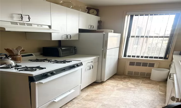 Kitchen featuring white cabinetry, radiator heating unit, and white gas range oven