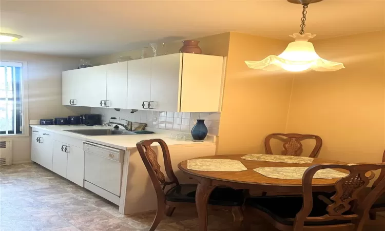 Kitchen featuring decorative backsplash, white dishwasher, sink, decorative light fixtures, and white cabinets