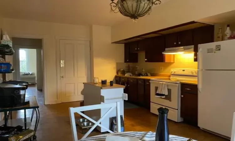 Kitchen with dark brown cabinets, white appliances, tasteful backsplash, and an inviting chandelier