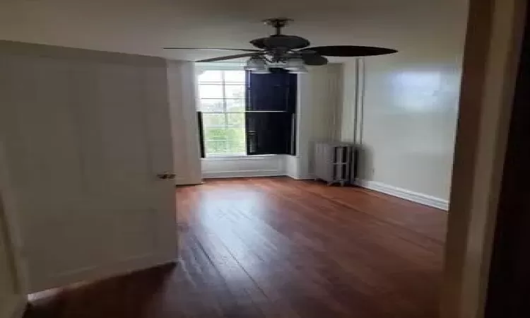 Unfurnished room featuring ceiling fan, radiator heating unit, and dark wood-type flooring