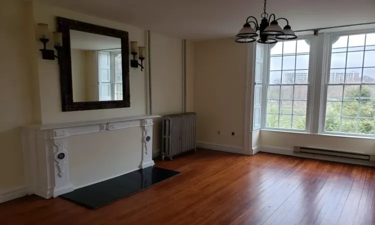 Unfurnished dining area with wood-type flooring, an inviting chandelier, radiator, and a baseboard heating unit