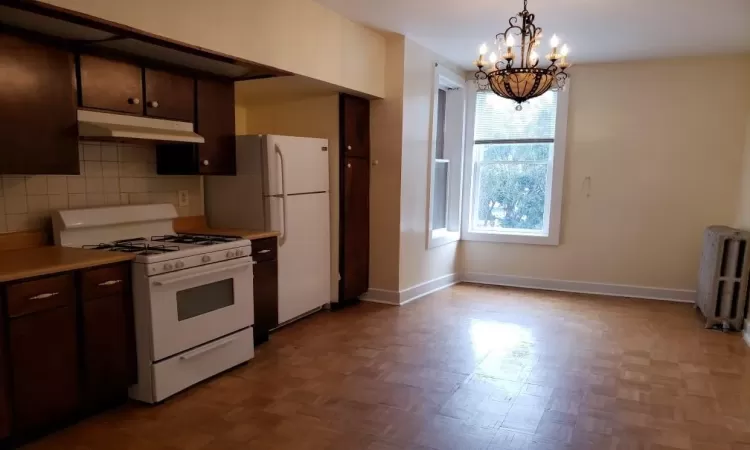 Kitchen featuring tasteful backsplash, white appliances, dark brown cabinetry, a notable chandelier, and radiator heating unit