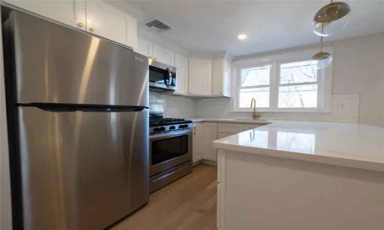 Kitchen with white cabinetry, sink, stainless steel appliances, tasteful backsplash, and light hardwood / wood-style flooring