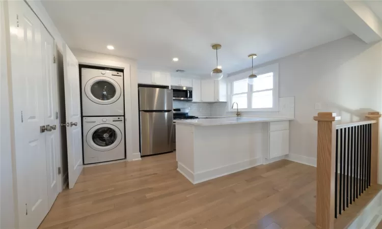 Kitchen featuring stacked washer and clothes dryer, white cabinets, light wood-type flooring, kitchen peninsula, and stainless steel appliances