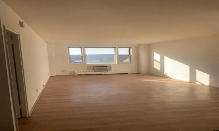 Empty room with an AC wall unit, hardwood / wood-style floors, and a baseboard heating unit