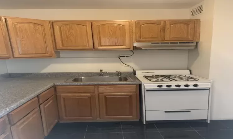 Kitchen with white range oven, sink, and dark tile patterned flooring