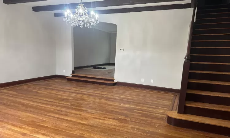 Unfurnished living room with a notable chandelier, a stone fireplace, wood-type flooring, and radiator