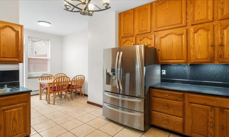 Kitchen with decorative backsplash, baseboard heating, light tile patterned floors, an inviting chandelier, and stainless steel fridge with ice dispenser