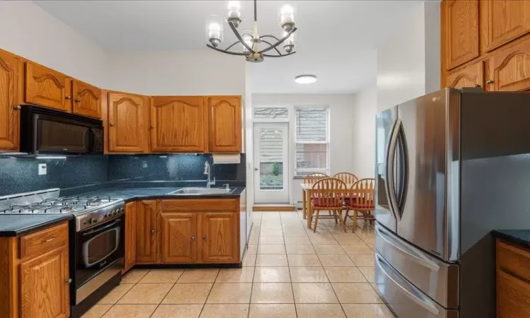 Kitchen featuring sink, stainless steel appliances, an inviting chandelier, backsplash, and light tile patterned flooring