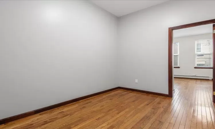 Empty room featuring hardwood / wood-style floors and a baseboard radiator