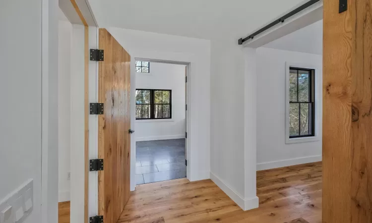 Hallway featuring light wood-type flooring, a barn door, and a healthy amount of sunlight