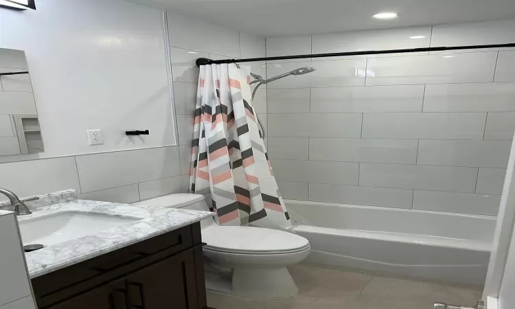 Full bathroom with tile patterned floors, shower / bath combination with curtain, toilet, vanity, and tile walls