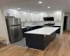 Kitchen featuring appliances with stainless steel finishes, light wood-type flooring, sink, white cabinets, and a kitchen island