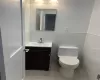 Bathroom featuring tile patterned floors, vanity, tile walls, and toilet