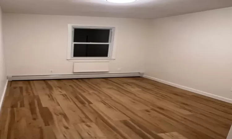 Unfurnished room featuring hardwood / wood-style floors and a baseboard heating unit