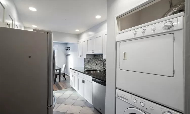 Kitchen featuring appliances with stainless steel finishes, sink, light tile patterned floors, stacked washer and clothes dryer, and white cabinetry