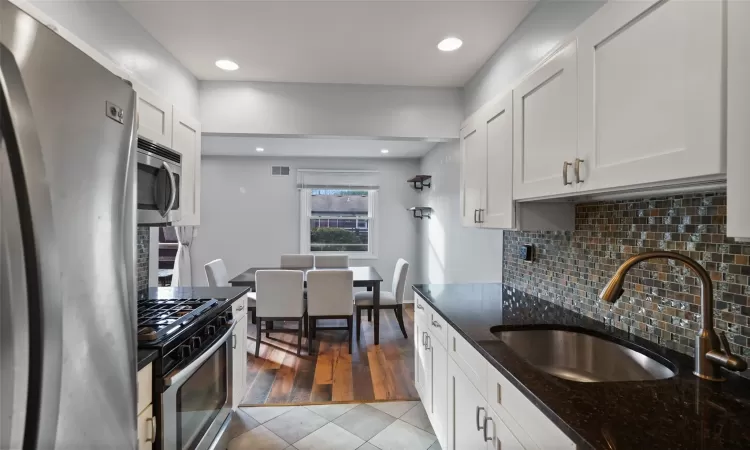 Kitchen featuring sink, light hardwood / wood-style flooring, dark stone countertops, appliances with stainless steel finishes, and white cabinetry