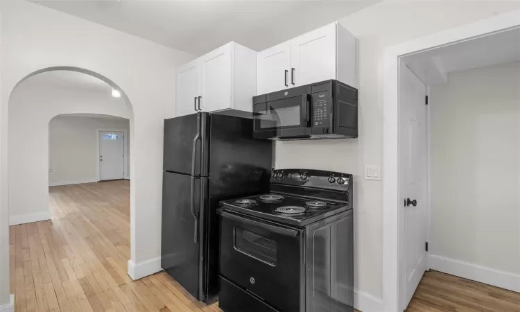 Kitchen featuring white cabinetry, black appliances, and light hardwood / wood-style floors