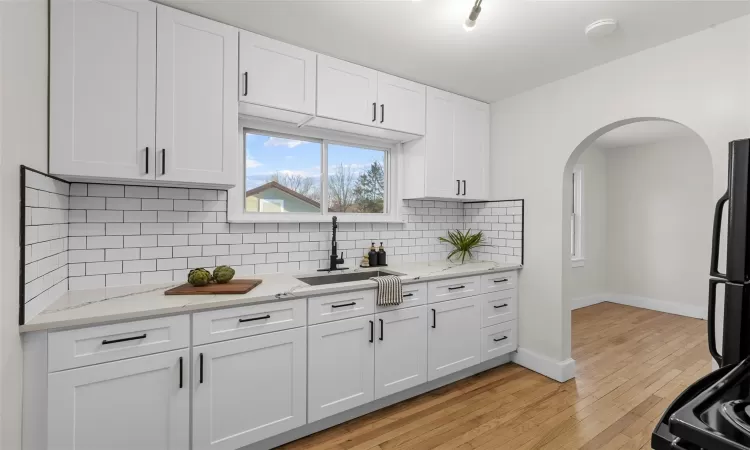 Kitchen featuring backsplash, black fridge, sink, light wood-type flooring, and white cabinetry