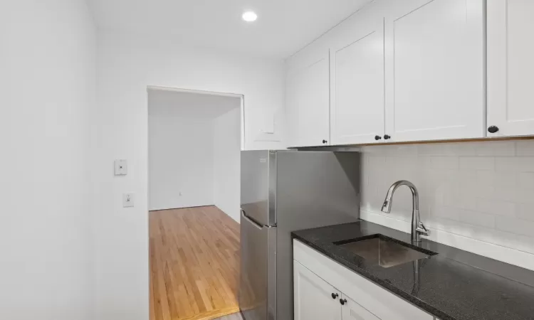 Kitchen with stainless steel refrigerator, white cabinetry, sink, and light hardwood / wood-style flooring