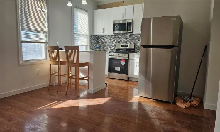 Kitchen with a kitchen bar, decorative backsplash, light wood-type flooring, stainless steel appliances, and white cabinetry