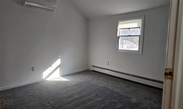 Spare room featuring a wall mounted AC, dark carpet, and baseboard heating