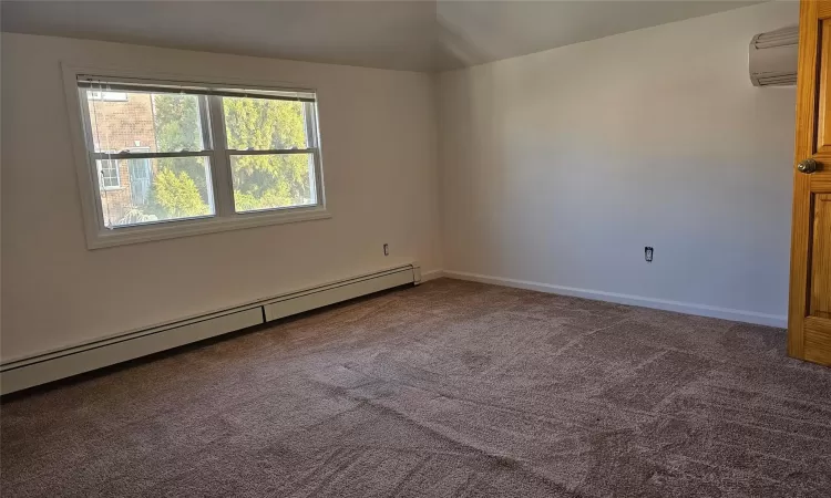 Carpeted spare room featuring a wall mounted AC and a baseboard radiator