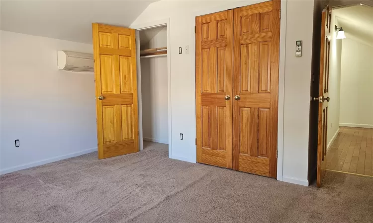 Unfurnished bedroom featuring carpet flooring, a closet, and a wall mounted air conditioner