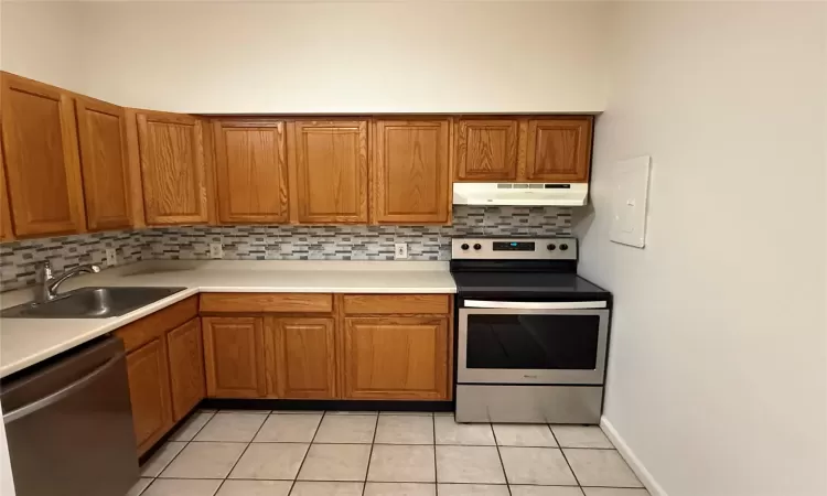 Kitchen with appliances with stainless steel finishes, tasteful backsplash, light tile patterned floors, and sink