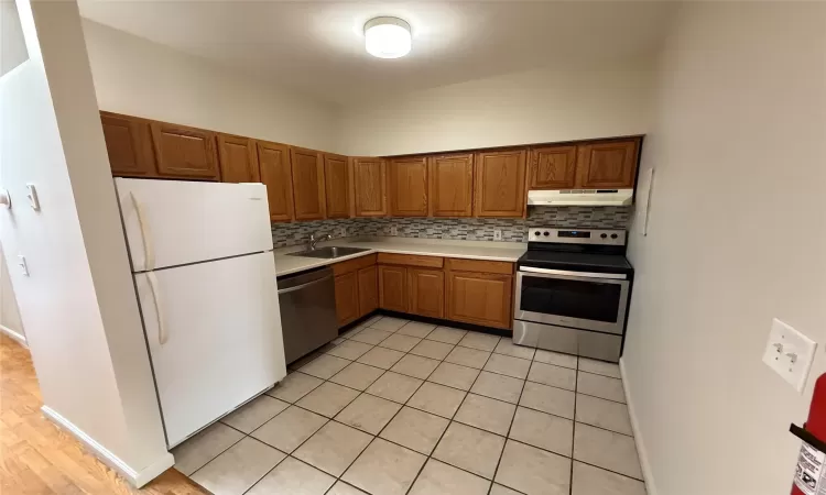 Kitchen featuring light tile patterned flooring, appliances with stainless steel finishes, decorative backsplash, and sink