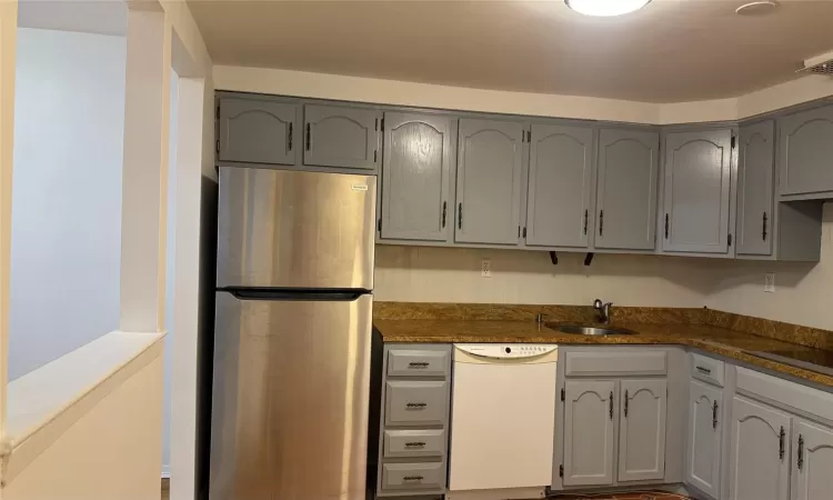 Kitchen with white dishwasher, sink, stainless steel fridge, gray cabinets, and stovetop