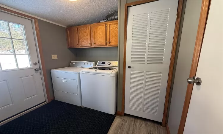 Clothes washing area with cabinets, separate washer and dryer, a textured ceiling, and light hardwood / wood-style flooring