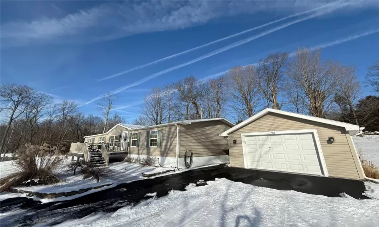 Snow covered property with an outbuilding, a garage, and a wooden deck