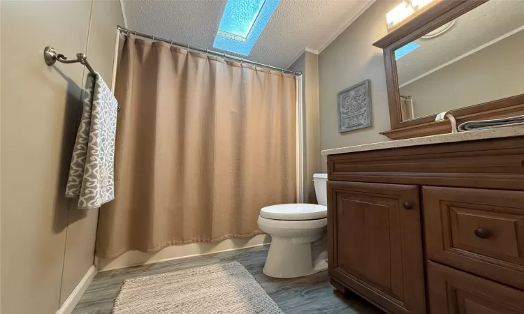 Full bathroom with a skylight, shower / bath combo, hardwood / wood-style floors, a textured ceiling, and vanity