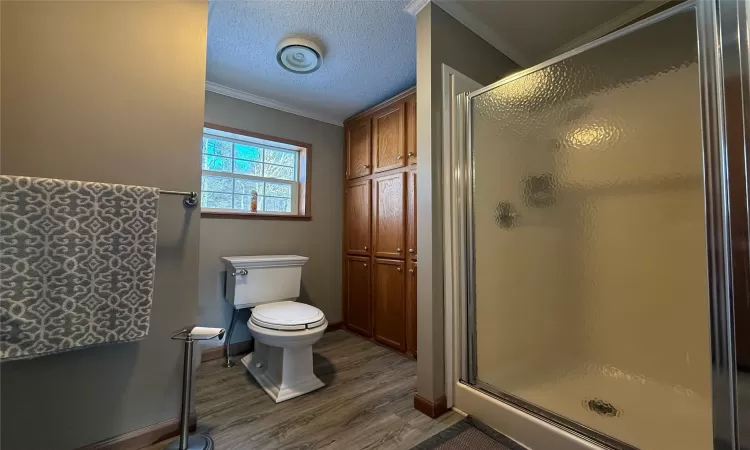 Bathroom with an enclosed shower, a textured ceiling, crown molding, hardwood / wood-style flooring, and toilet