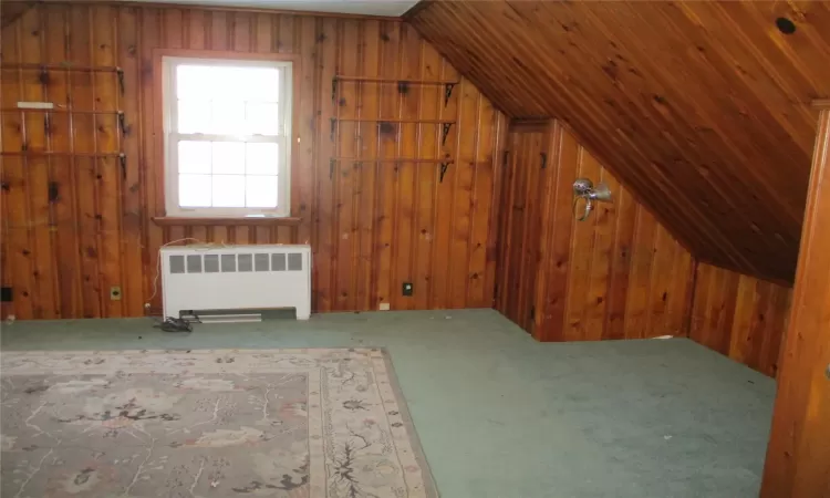 Bonus room featuring carpet flooring, vaulted ceiling, radiator, and wooden walls