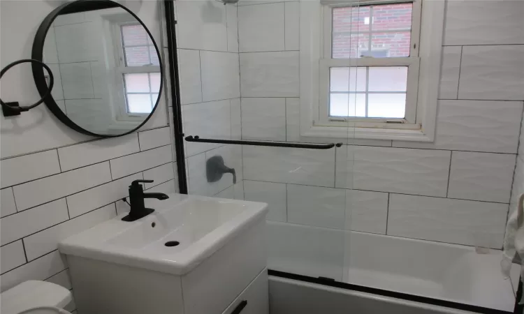 Full bathroom featuring backsplash, combined bath / shower with glass door, toilet, vanity, and tile walls