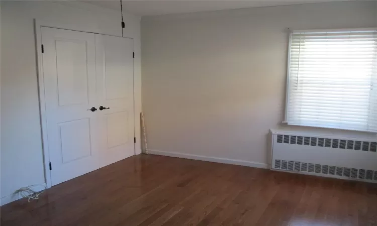 Empty room featuring dark hardwood / wood-style flooring, radiator, and ornamental molding