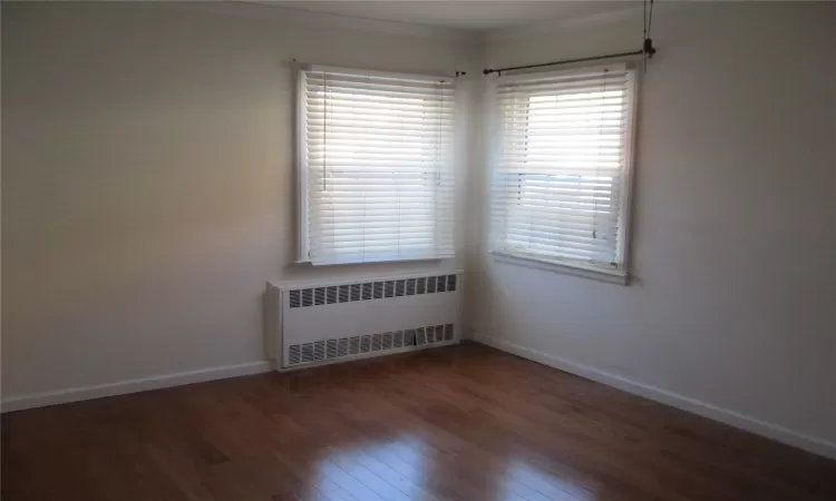 Spare room featuring dark hardwood / wood-style floors, radiator heating unit, and crown molding