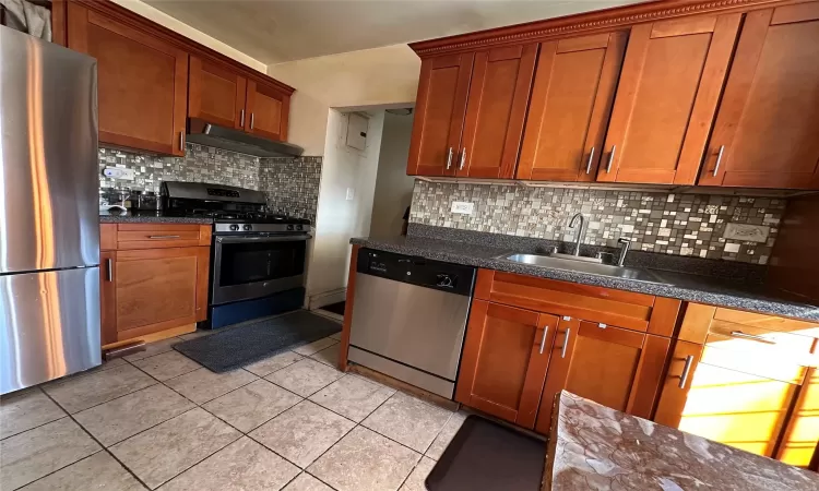 Kitchen featuring radiator heating unit, sink, stainless steel dishwasher, backsplash, and light tile patterned flooring