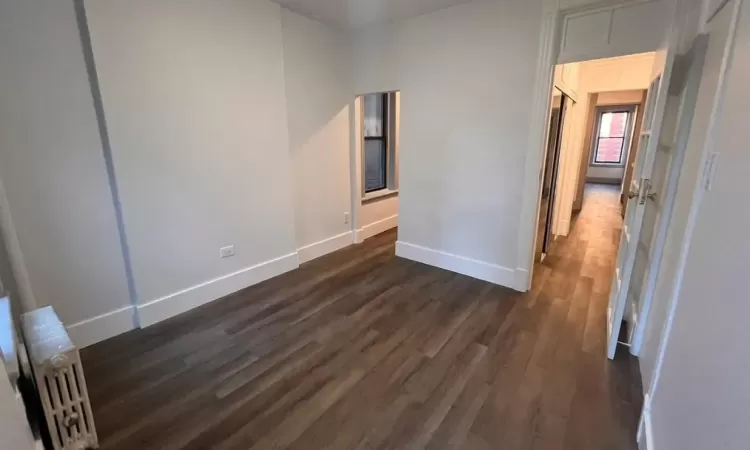 Unfurnished bedroom featuring radiator and dark hardwood / wood-style flooring