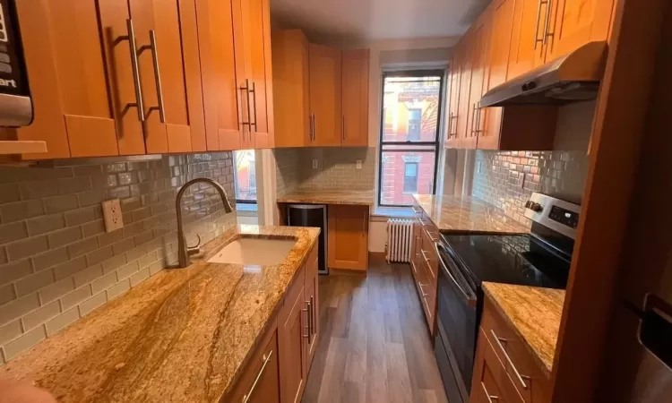 Kitchen featuring stainless steel range with electric stovetop, backsplash, radiator heating unit, and sink