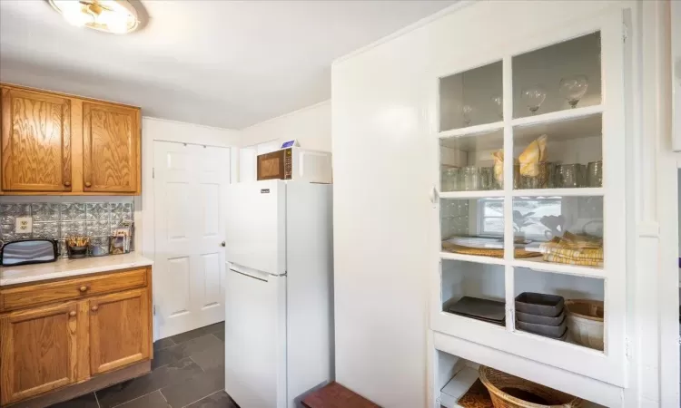 Kitchen with white fridge, dark tile patterned floors, and tasteful backsplash