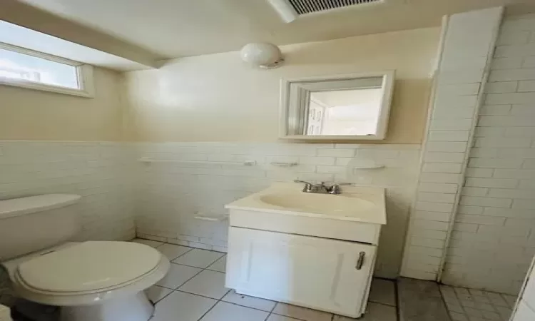 Bathroom featuring tile patterned flooring, vanity, toilet, and tile walls