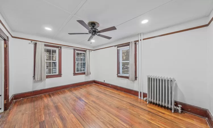 Empty room with wood-type flooring, radiator, and ceiling fan