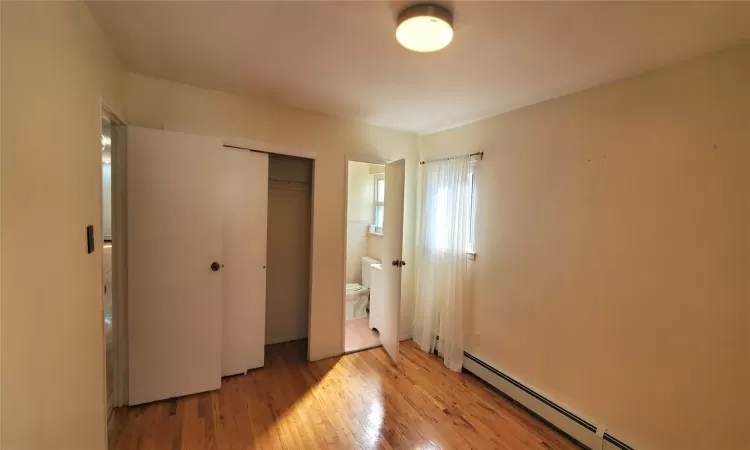 Unfurnished bedroom featuring a baseboard heating unit, light hardwood / wood-style flooring, a closet, and ensuite bath