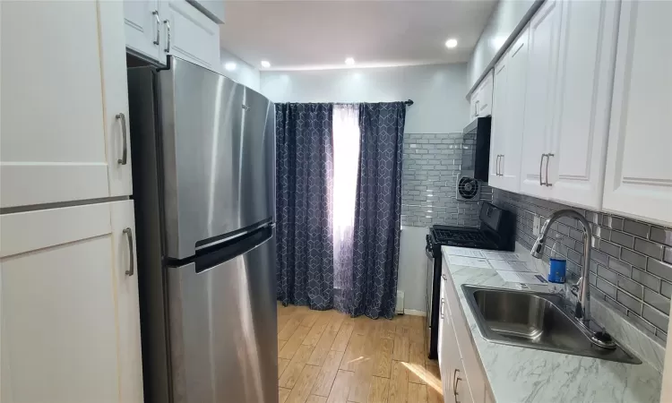 Kitchen with backsplash, sink, light hardwood / wood-style flooring, white cabinetry, and stainless steel appliances