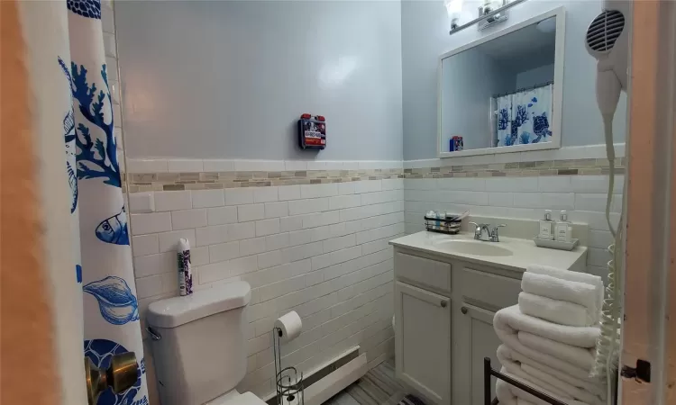 Bathroom featuring vanity, a baseboard radiator, toilet, and tile walls